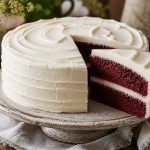 Two-layer red velvet cake with cream cheese frosting and a slice showing the crimson crumb