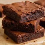 Stack of chewy classic fudge brownies with a shiny crackly top on parchment