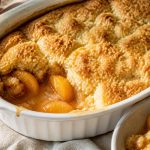 Southern peach cobbler in a baking dish with biscuit topping and bubbling peach juices