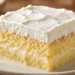 Slice of tres leches cake soaked with three milks and topped with whipped cream